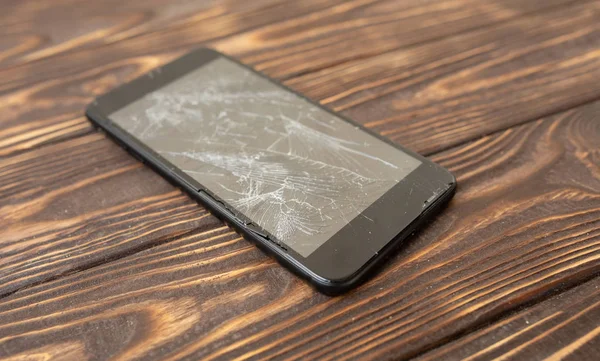 Modern broken mobile phone on old wooden background