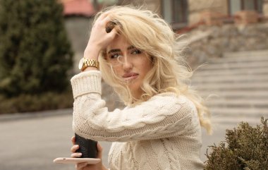 Büyük bir şehirde modern genç bir kadın. Cep telefonu ve fincan kahve ile Sarışın kadın.