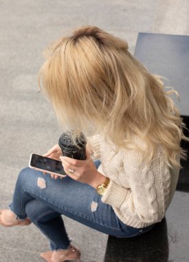 Büyük bir şehirde modern genç bir kadın. Cep telefonu ve fincan kahve ile Sarışın kadın.