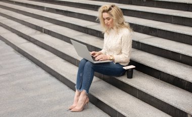Genç çekici iş kadını merdivenlerde oturan ve modern dizüstü bilgisayar kullanarak
