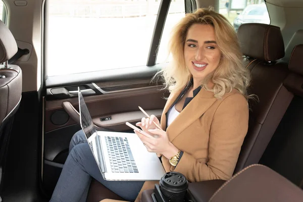 Beautiful business woman sitting in back seat of car and work on laptop.