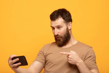 Sarı arka plan üzerinde duran heyecanlı bir adamın portresi, cep telefonu tutan, kutlayan