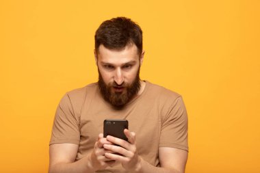 Sarı arka plan üzerinde izole cep telefonu bakarak sürpriz bir rahat adam Portresi