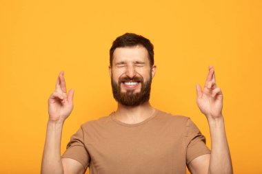Mutlu pozitif sakallı adam parmakları haçlar, zevkle gözleri kapatır, iyi haber işitme tahmin, izole renk arka plan. Mutlu erkek hayallerinin gerçek olduğuna sevinir. Heyecan kavramı
