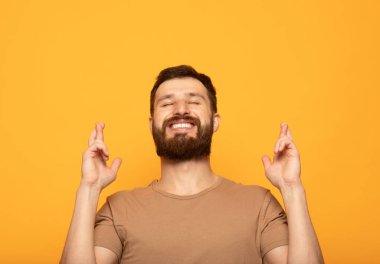 Mutlu pozitif sakallı adam parmakları haçlar, zevkle gözleri kapatır, iyi haber işitme tahmin, izole renk arka plan. Mutlu erkek hayallerinin gerçek olduğuna sevinir. Heyecan kavramı