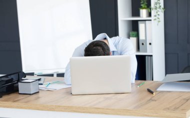 working man exhausted and sleeping on laptop with mobile phone at wooden workspace