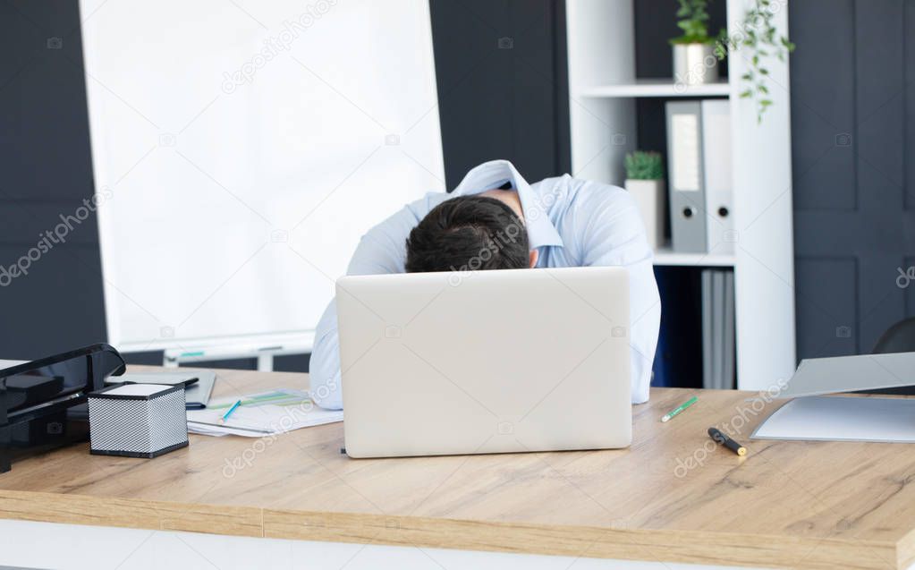 Working man exhausted and sleeping on laptop with mobile phone at wooden workspace