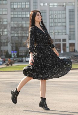Moda stil portre genç mutlu gülümseyen güzel zarif kadının siyah elbiseli şehrin sokaklarında yürüyüş.
