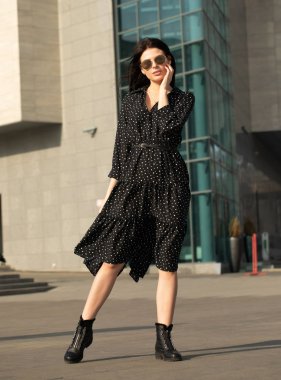 Moda stil portre genç mutlu gülümseyen güzel zarif kadının siyah elbiseli şehrin sokaklarında yürüyüş.
