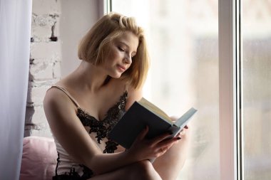 Güzel mutlu genç güzel kadın evde kitap okuma oturan Fotoğraf 