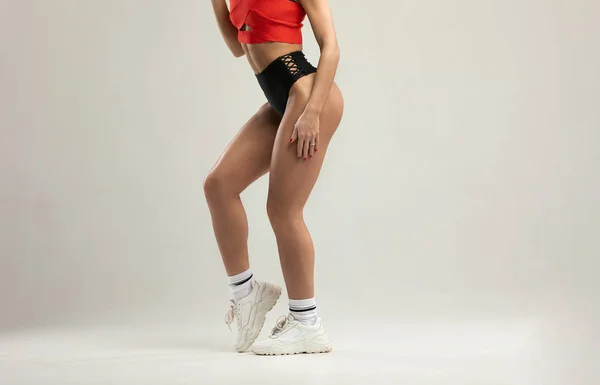 Happy young woman in sports clothing. Muscular fitness model on grey background. Red and black clothes.