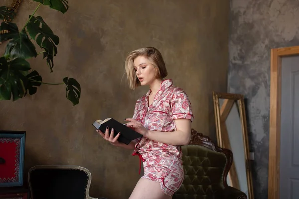 自宅で読書本に座っている美しい幸せな若いかわいい女性の写真 — ストック写真