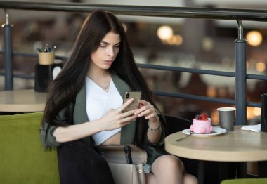 Bir kafedeki masada otururken bir parça kek yiyip kahve içen mutlu bir kadının portresi.