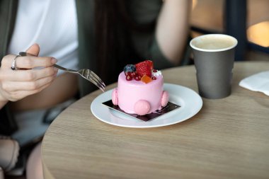 Bir kafedeki masada otururken bir parça kek yiyip kahve içen mutlu bir kadının portresi.