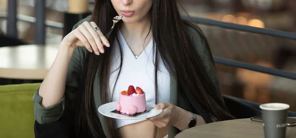 一个快乐的女人坐在室内咖啡馆的桌子边 一边吃着一块蛋糕一边喝咖啡的画像 — 图库照片