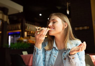 Restoranda pizza yiyen kot ceket komik sarışın kız.