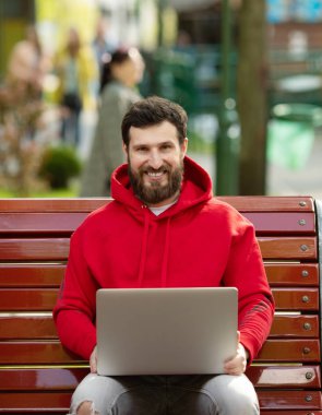 Pozitif Kafkas sakallı adam açık havada çalışan genel dizüstü bilgisayar önünde oturuyor. Açık dizüstü bilgisayar ile parkta oturan serbest çalışma