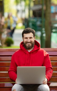 Pozitif Kafkas sakallı adam açık havada çalışan genel dizüstü bilgisayar önünde oturuyor. Açık dizüstü bilgisayar ile parkta oturan serbest çalışma