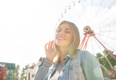 Arka planda park dönme dolap uzağa bakarak gülümseyen rahat genç sarışın yakın. Güneş ışığında mutlu kadın.