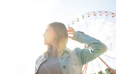 Arka planda park dönme dolap uzağa bakarak gülümseyen rahat genç sarışın yakın. Güneş ışığında mutlu kadın.