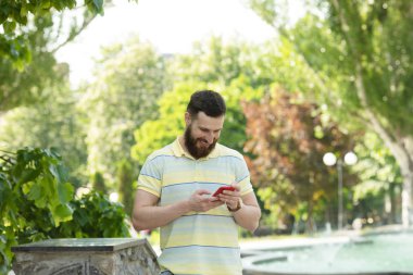 Parkta akıllı telefon kullanarak çizgili t-shirt genç sakallı adam