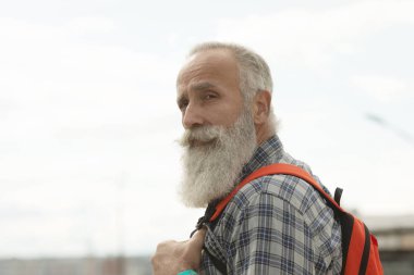 Şehirde yürüyen rahat giysiler ve kırmızı sırt çantası sakallı ve bıyıklı Hipster yaşlı adam