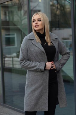 Gri ceketli zarif sarışın kadın şehirde poz, arka planda modern bina.