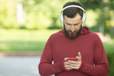 Parkta eğitim sırasında akıllı telefon kullanan kulaklık ve spor giyim sakallı adam