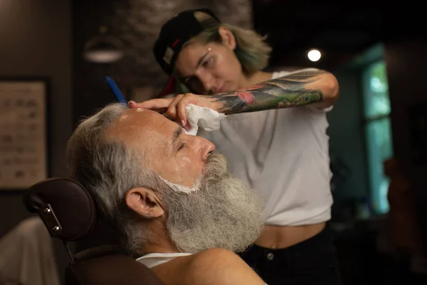 Master cuts hair and beard of men in the barbershop, hairdresser makes hairstyle for  old man.