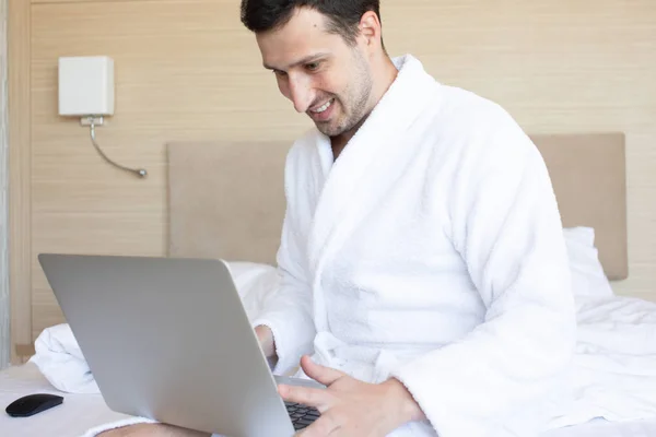 Νέος Άντρας Μπουρνούζι Χρησιμοποιώντας Φορητό Υπολογιστή Στο Υπνοδωμάτιο Πρωί — Φωτογραφία Αρχείου