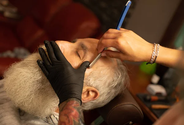 Closeup of barber hands shaving man\'s stubble with straight razors at barber shop.