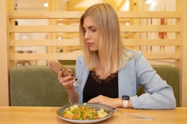 Kafeteryada haşlanmış sebze yiyen muhteşem gülümseyen genç kadın. 