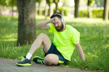 Parkta eğitim den sonra dinlenmiş kulaklık ve spor giyim genç yorgun sakallı adam