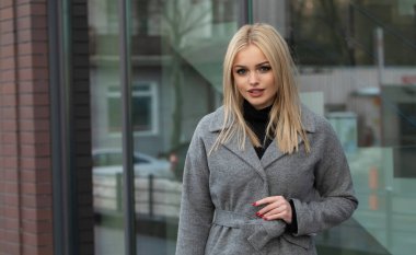 Gri ceketli zarif sarışın kadın şehirde poz, arka planda modern bina.