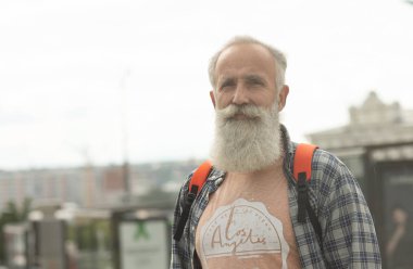 Şehirde yürüyen rahat giysiler ve kırmızı sırt çantası sakallı ve bıyıklı Hipster yaşlı adam