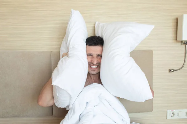 愤怒的男人早上在床上用枕头捂住耳朵 — 图库照片