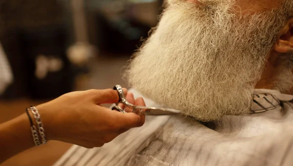 Cropped view of woman barber trimming man beard with scissors.