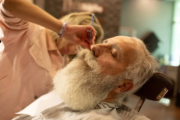 Closeup of barber hands shaving man\'s stubble with straight razors at barber shop.