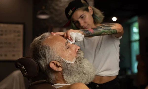 Master cuts hair and beard of men in the barbershop, hairdresser makes hairstyle for  old man.
