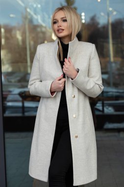 Beyaz ceketli zarif sarışın kadın şehirde poz, arka planda modern bina.