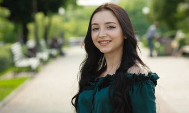 Parktaki kameraya gülümseyen genç, güzel esmer kadın.