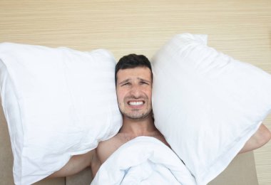 Sabah yatakta oturan yastıklarla kulaklarını kapatan kızgın adam