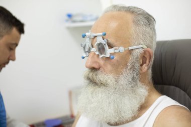 Doktor göz doktoru, özel tıbbi aletle hastayı muayene ediyor. Gözlüklü uzman, optalmoloji ekipmanında kıdemli adam..