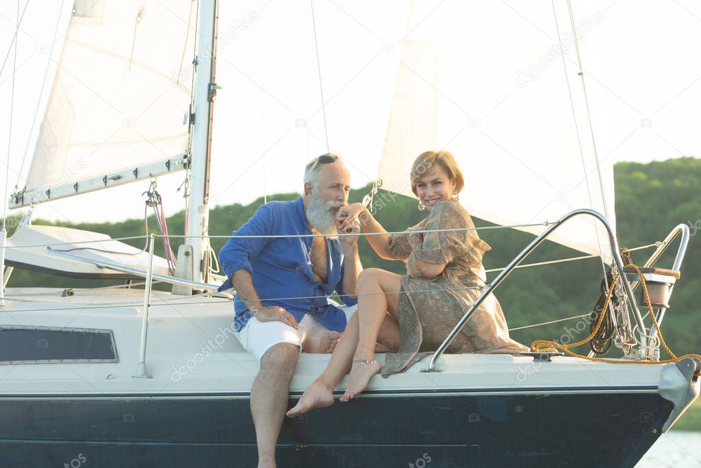 A happy senior couple sailing and sitting at the wheel of a sail boat on lake.