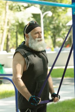 Esnek direniş bandıyla fitness egzersizleri yapan yaşlı bir adam. Lastik bantla sakallı son sınıf eğitimi. Spor, spor, sağlıklı yaşam tarzı konsepti.