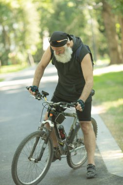 Sakallı olgun atletik adam renkli bir yaz parkında bisikletle dikiliyor..