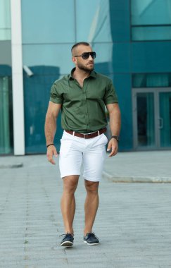 Güneş gözlüklü ve gömlekli kendine güvenen yakışıklı bir adam. Erkek güzelliği, moda. Açık havada portre.