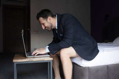 Takım elbiseli ve iç çamaşırlı mutlu iş adamı otel odasında dizüstü bilgisayar kullanıyor..