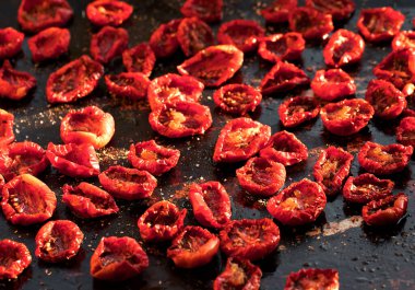 Küçük parçalar halinde güneşte kurutulmuş domatesler koyu arkaplanda metal bir kapta yatıyor. Sağlıklı yemek..