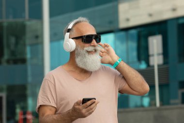 Yetişkin hippi adam şehirde yürürken kulaklıkla müzik dinleyerek eğleniyor.